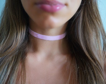 May include: A close-up of a person wearing a light pink choker necklace.