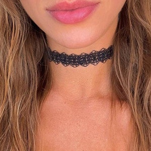 May include: A close-up of a person wearing a black lace choker necklace. The choker is delicate and has a feminine design.