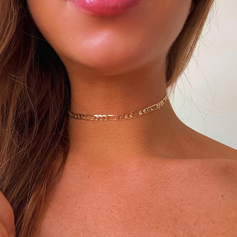 May include: A gold chain choker necklace on a person's neck.