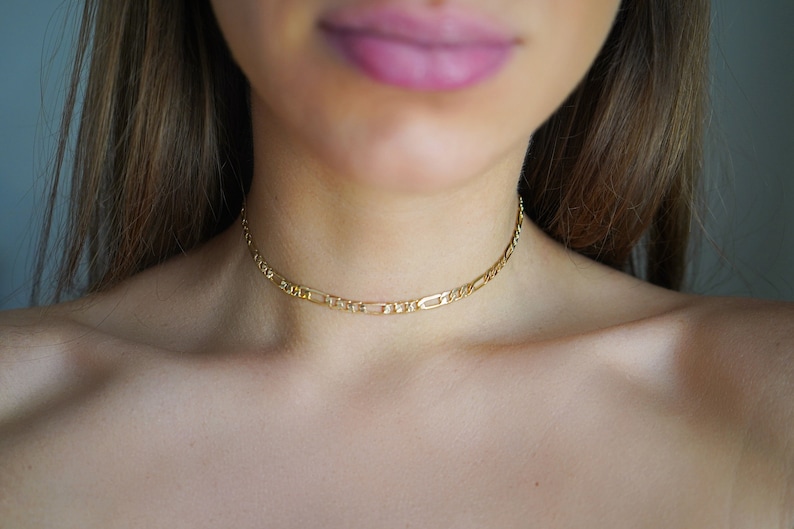 May include: A gold chain choker necklace on a person's neck.