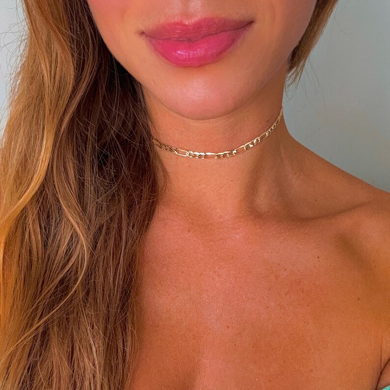 May include: A gold chain choker necklace on a person's neck. The chain is a simple, flat design.