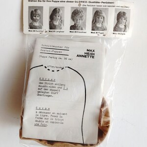 May include: A vintage doll pattern by Max Heidi Annette, packaged in a clear plastic bag. The pattern includes instructions in German and French, with a diagram of the doll's body. The package also features images of doll wigs.