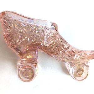 May include: A pink glass slipper with a detailed starburst pattern. The decorative shoe has a high heel and a rounded toe. The glass has an iridescent quality, reflecting light. The slipper is likely a decorative item.