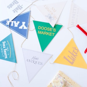 May include: A string of triangular pennants with various text, including "Yale", "Doose's Market", and "Luke's". The pennants are in different colors and are strung together with gold string. A red licorice rope and frosted cookies are also present.