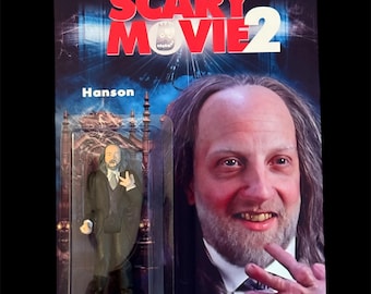 Op de afbeelding: Scary Movie 2 actiefiguur van Hanson in een plastic verpakking. De verpakking heeft de filmtitel in rood en wit. De figuur draagt een zwart pak, een wit overhemd en een stropdas.
