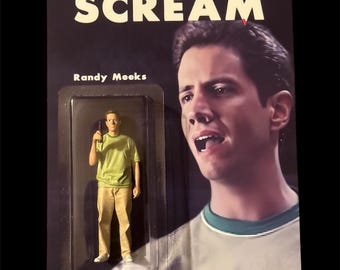 May include: A Scream action figure featuring Randy Meeks, packaged on a black card. The card has the word "SCREAM" in large white letters. The figure is in a clear plastic case. The figure is wearing a green shirt and khaki pants.