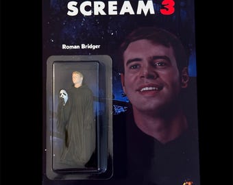 May include: A Scream 3 action figure featuring Roman Bridger in a black robe and Ghostface mask. The packaging includes the movie title and a portrait of Roman Bridger. The background is dark with a starry design.