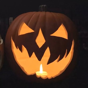 Może przedstawiać: Wyrzeźbiona dynia z twarzą jack-o'-lantern, oświetlona od wewnątrz małą świecą. Dynia jest pomarańczowa z trójkątnymi oczami, nosem w kształcie rombu i postrzępionymi ustami. Tło jest ciemne.