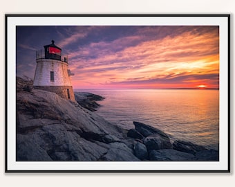 May include: A framed print of a lighthouse on a rocky coastline at sunset. The white lighthouse has a red light at the top. The sky is filled with orange, pink, and purple hues. The ocean is calm.