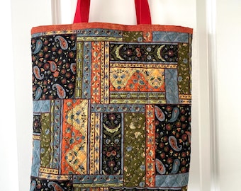May include: A quilted tote bag with a patchwork design featuring paisley and floral patterns in black, orange, green, and blue. The bag has red handles and trim.