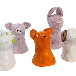 Könnte beinhalten: Fünf Keramik-Tierfiguren, jede mit einem anderen Tierkopf und einem weißen Körper. Die Tiere sind ein Schwein, ein Schaf, ein Kaninchen, ein Hund und eine Katze. Das Schwein ist lila, das Schaf ist weiß, das Kaninchen ist lila, der Hund ist weiß mit braunen Ohren und die Katze ist orange.