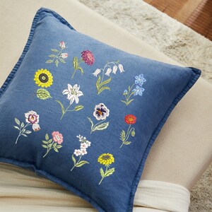 Puede incluir: Una almohada azul con dise&ntilde;os florales bordados en varios colores, incluyendo amarillo, rojo, rosa, blanco y verde.