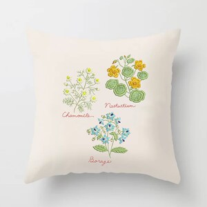 Pu&ograve; includere: Un cuscino bianco con immagini ricamate di tre fiori: camomilla, nasturzio e borragine. I fiori sono ricamati in tonalit&agrave; di verde, giallo, blu e bianco. I nomi dei fiori sono scritti in corsivo sotto ogni immagine.