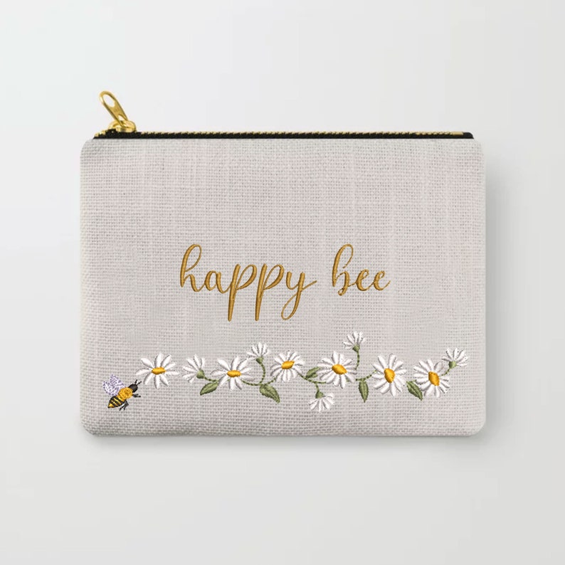 May include: A gray zippered pouch with a white daisy chain and a bee embroidered on it. The text "happy bee" is embroidered in gold on the pouch.