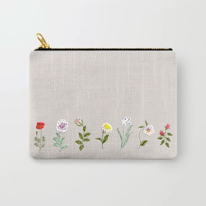 Puede incluir: Una bolsa de cremallera gris con una tela blanca similar al lino. La bolsa tiene una fila de flores bordadas en varios colores, incluyendo rojo, rosa, amarillo, azul y verde.