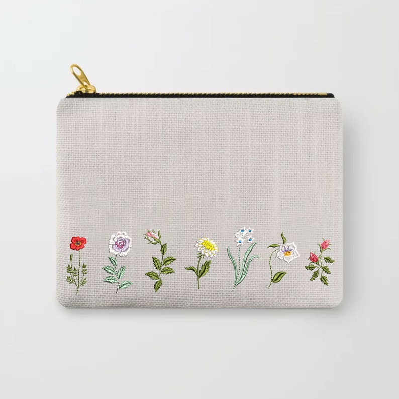 Puede incluir: Una bolsa de cremallera gris con una tela blanca similar al lino. La bolsa tiene una fila de flores bordadas en varios colores, incluyendo rojo, rosa, amarillo, azul y verde.