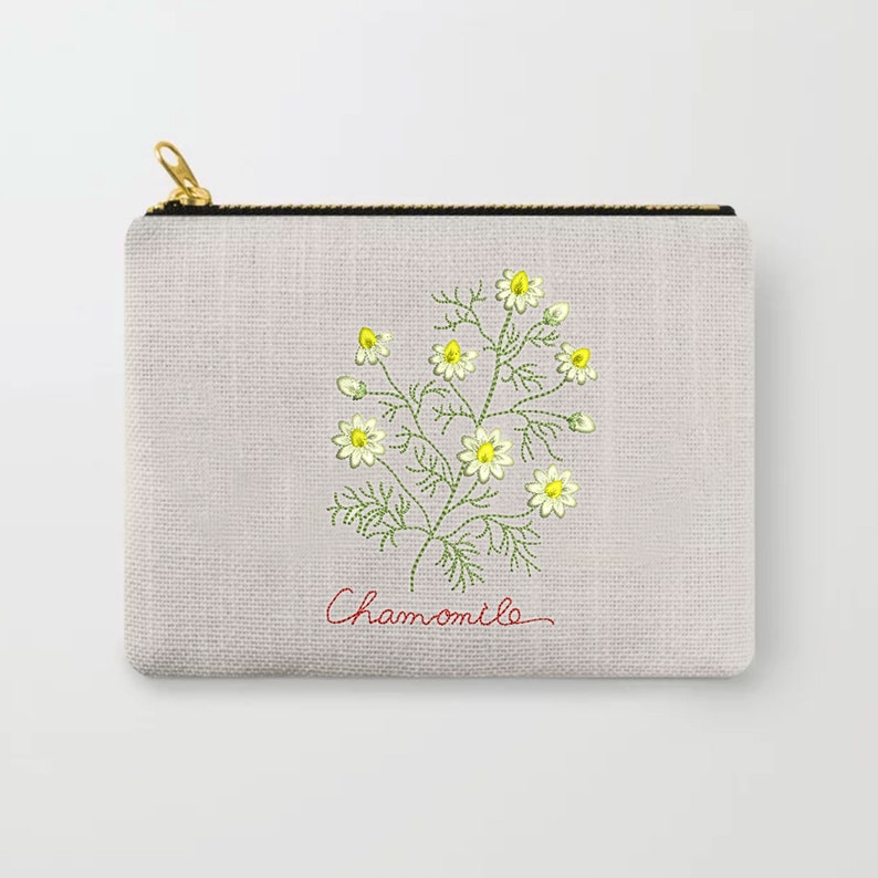 Pu&ograve; includere: Una pochette con cerniera in tela bianca con un motivo di camomilla ricamato in verde e giallo e la parola "Chamomile" in corsivo rosso.