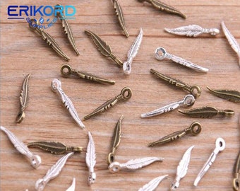 Puede incluir: Una colección de abalorios de plumas de plata y bronce con un bucle en la parte superior. Los abalorios están esparcidos sobre una superficie de madera.