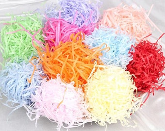 May include: A variety of colorful shredded paper, also known as crinkle paper or tissue paper shreds, in a bowl. The colors include light green, light blue, light pink, orange, yellow, and red.