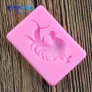 Puede incluir: Un molde de silicona rosa con un diseño de gallo. El molde rectangular tiene esquinas redondeadas y el gallo está representado de forma detallada y estilizada. El texto "ERIKORD" es visible en la esquina superior izquierda.