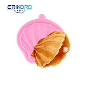 Könnte beinhalten: Rosa Silikonform in Form einer Muschel mit einer kleineren Muschel im Inneren, die eine weiße Perle enthält. Die Form ist zum Herstellen von Kuchendekorationen oder anderen essbaren Leckereien.