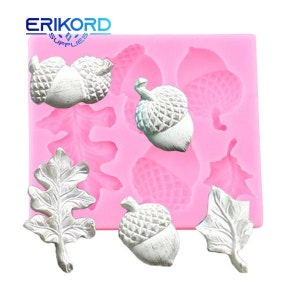 Op de afbeelding: Een roze siliconen mal met eikel- en bladvormen. De eikels en bladeren zijn wit en hebben gedetailleerde texturen. De mal heeft de tekst "ERIKORD SUPPLIES" in blauw en wit in de linkerbovenhoek.