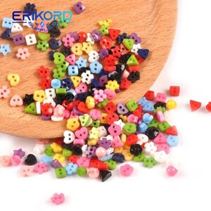 May include: A large assortment of colorful plastic buttons in various shapes, including circles, hearts, stars, and triangles. The buttons are scattered on a wooden surface and a white background.