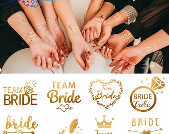 May include: Gold temporary tattoos with various designs for a bridal party. The designs include "Team Bride", "Bride Tribe", and a crown.