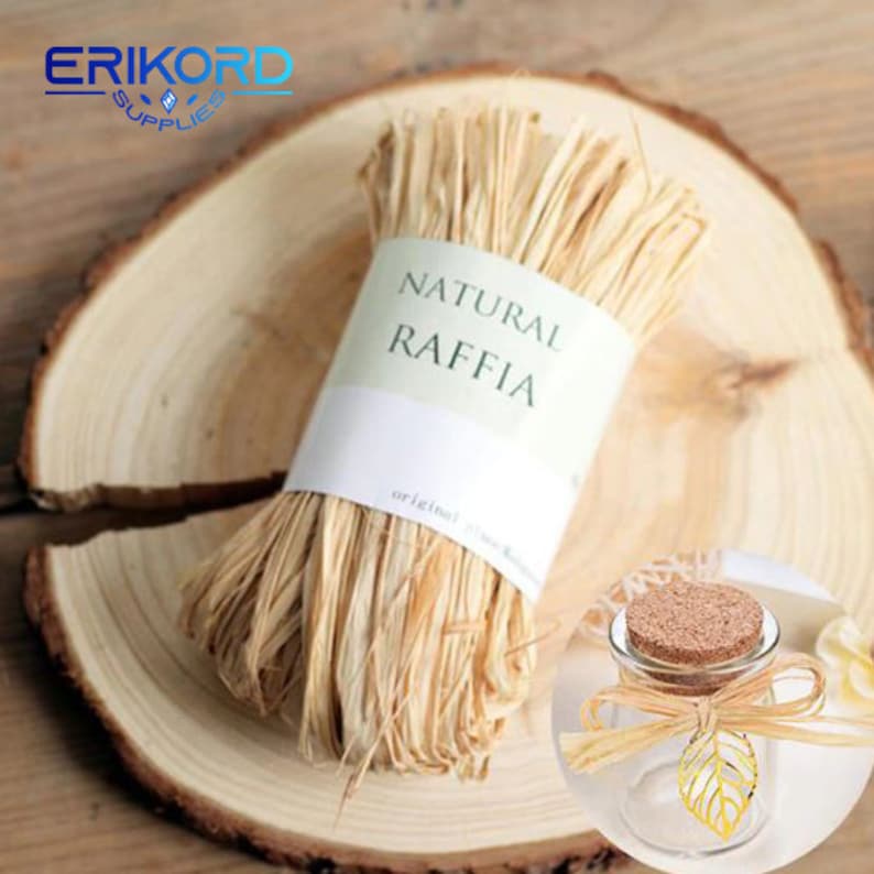May include: A roll of natural raffia fibre, a type of natural twine, is displayed on a wooden surface. The raffia is labelled "Natural Raffia" and "original".