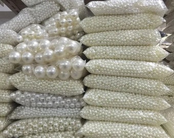 Puede incluir: Varias bolsas de cuentas de perlas blancas, algunas en hebras sueltas y otras en cuentas redondas más grandes.