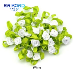 May include: A bunch of small, white satin flowers with green ribbon bows. The flowers are arranged in a pile, and the ribbon bows are tied around the stems of the flowers. The flowers are all the same size and shape, and they are all white. The ribbon bows are all the same size and shape, and they are all green.