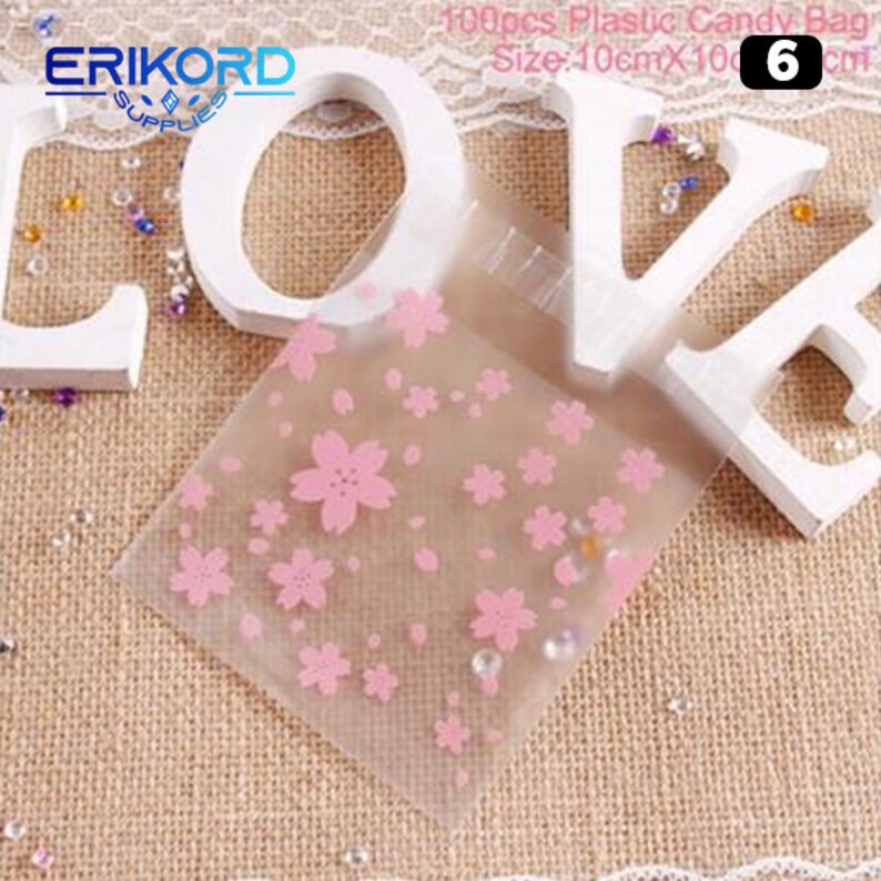 May include: 100 clear plastic candy bags with a pink cherry blossom design. The bags are 10 cm by 10 cm.