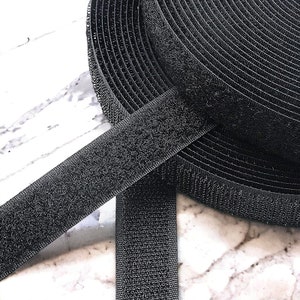 May include: Black hook and loop tape, also known as Velcro, is rolled up and laid out flat. The tape is made of a soft, fuzzy material and is designed to stick to itself.