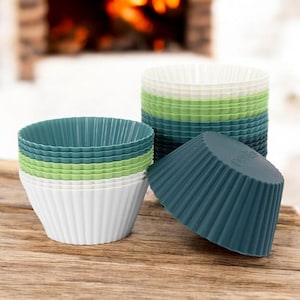 Könnte beinhalten: Ein Satz Silikon-Muffinformen in Weiß, Grün und Blau. Die Formen sind zu einem Turm gestapelt und eine Form liegt auf der Seite.