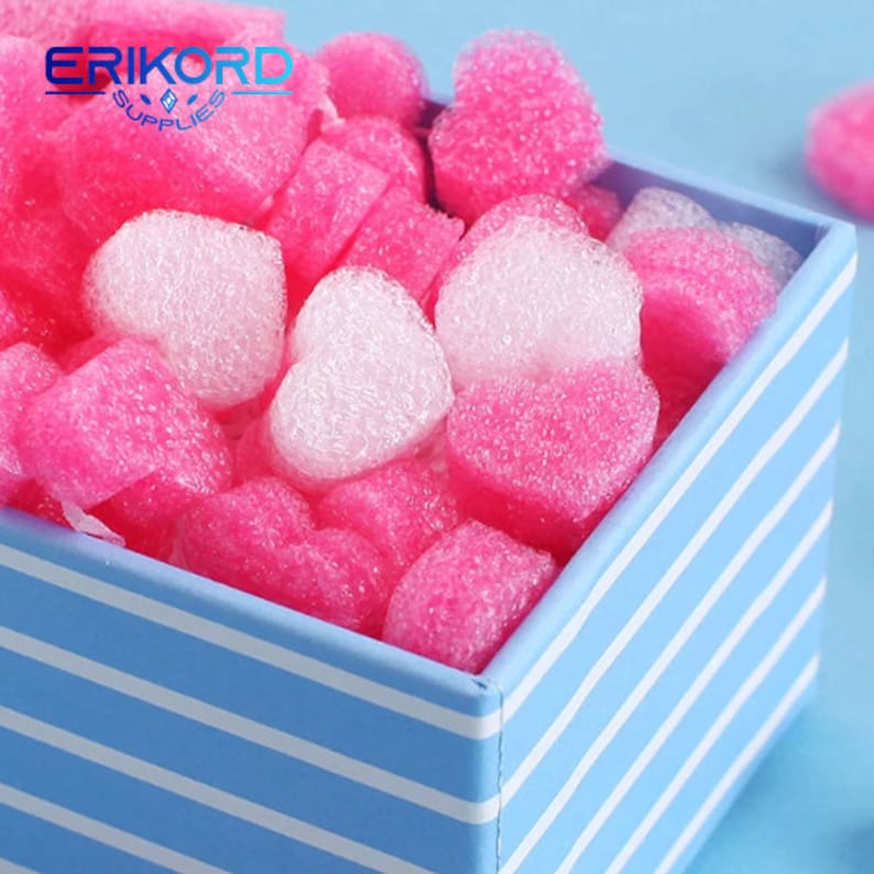 May include: A blue and white striped box filled with pink and white heart-shaped packing peanuts. The peanuts are made of foam and are used to protect fragile items during shipping.