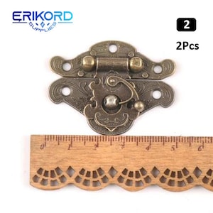 May include: Two antique-style bronze latch clasps with ornate designs. Each clasp has a hinged lid and a decorative knob. The clasps are shown against a wooden ruler for size reference. 2Pcs.