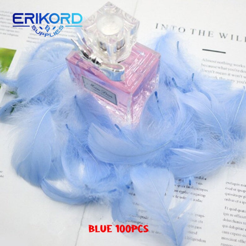 May include: A close-up of a pile of light blue feathers with a clear glass bottle of perfume in the centre. The bottle has a pink liquid and a silver bow. The text "BLUE 100PCS" is visible at the bottom of the image.