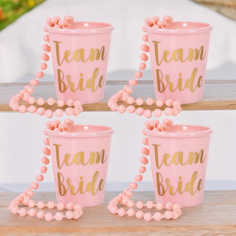 May include: Four pink plastic cups with gold lettering that says "Team Bride" and pink beaded necklaces.