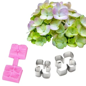 Puede incluir: Un arreglo de flores de hortensia frescas con pétalos verdes y morados. También hay un molde de silicona rosa y dos cortadores de galletas con forma de flor de acero inoxidable, ideales para hornear o manualidades.