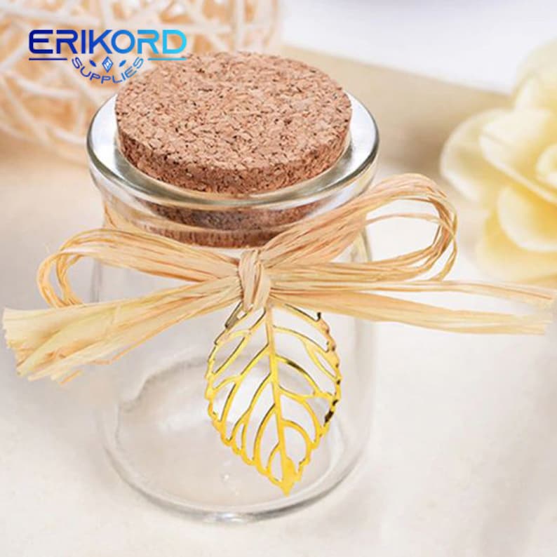 May include: A clear glass jar with a cork lid and a gold leaf charm. The jar is tied with a natural raffia ribbon and bow.