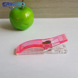 May include: A pink plastic fabric clip with a clear plastic base. The clip is open and ready to hold fabric.