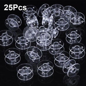 May include: A set of 25 clear plastic bobbins for sewing machines. The bobbins are stacked and scattered on a black background.