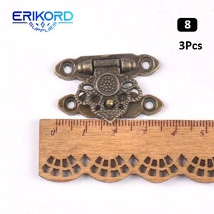 May include: Three antique brass-toned decorative clasps with intricate floral designs. Each clasp measures approximately 2 inches in length. The clasps are shown against a wooden ruler for scale.