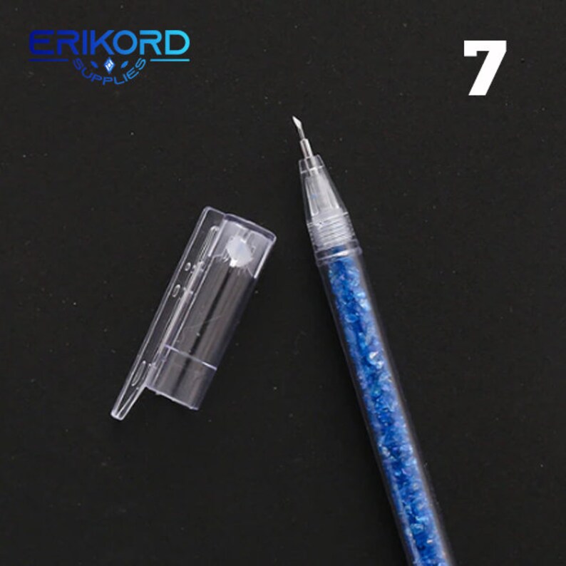 Puede incluir: Un bol&iacute;grafo de pl&aacute;stico transparente con un cuerpo de purpurina azul y un capuch&oacute;n de pl&aacute;stico transparente. El bol&iacute;grafo est&aacute; etiquetado con el n&uacute;mero "7".