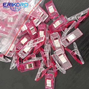 May include: A pile of pink and clear plastic fabric clips. The clips are used for holding fabric together while sewing.