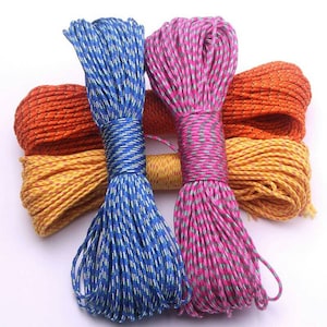 Puede incluir: Cuatro carretes de cuerda de paracord de colores. Los carretes están dispuestos en fila, con los carretes azul y rosa en la parte delantera y los carretes naranja y amarillo en la parte trasera. El paracord está hecho de un cordón de nylon delgado y duradero que se utiliza a menudo para manualidades, acampada y supervivencia.