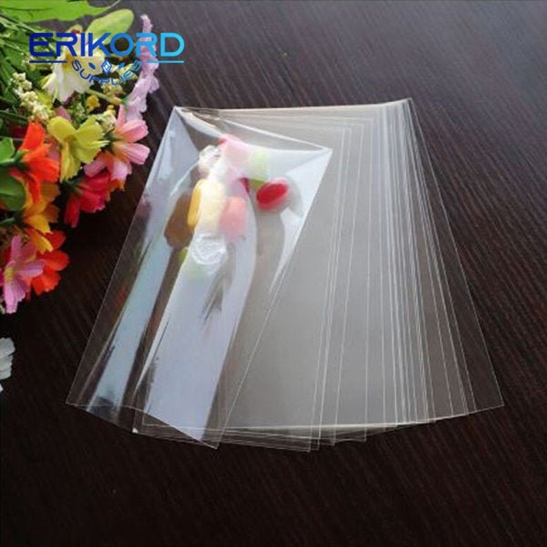 May include: A stack of clear plastic cellophane bags, ideal for packaging small items like sweets or jewellery. The bags are flat and have a smooth, transparent finish.
