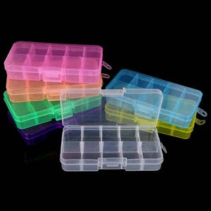Puede incluir: Seis cajas de almacenamiento de plástico transparente con divisores. Las cajas están apiladas una encima de la otra y son de diferentes colores: rosa, naranja, verde, morado, azul claro y amarillo.