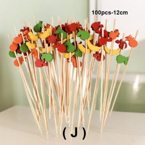 May include: A set of 100 wooden skewers with colorful fruit-shaped toppers. The skewers are 12 inches long and come in a variety of colors, including red, yellow, green, and orange. The fruit toppers are made of wood and are shaped like bananas, apples, strawberries, and pineapples. 100pcs-12cm (J)