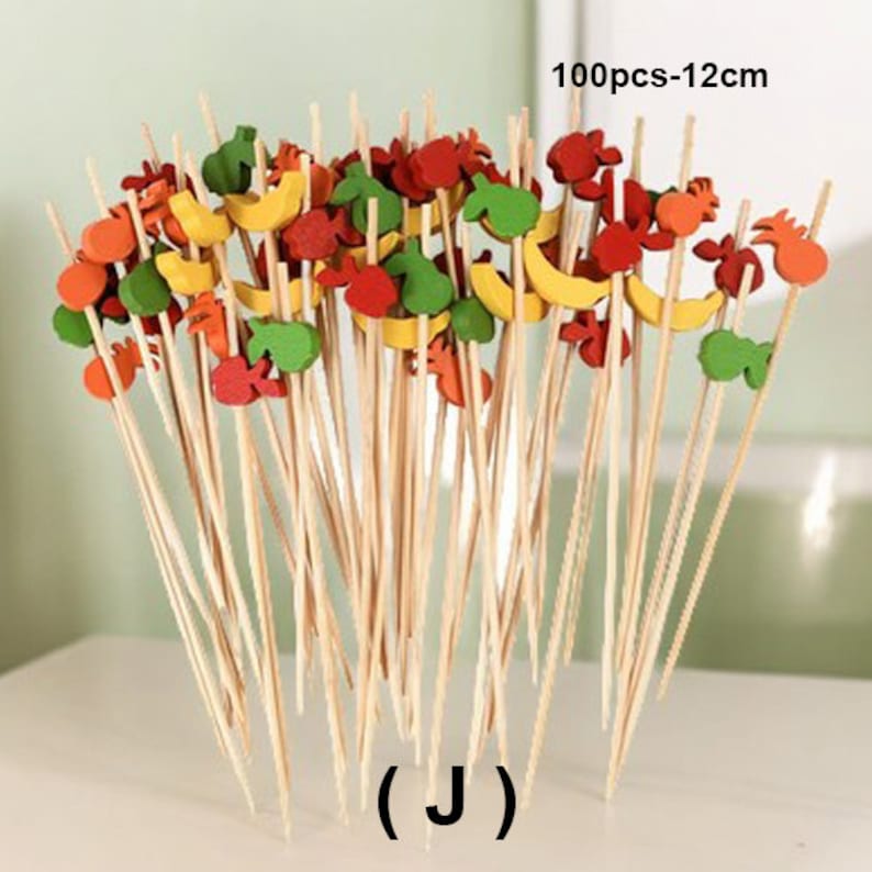 May include: A set of 100 wooden skewers with colorful fruit-shaped toppers. The skewers are 12 inches long and come in a variety of colors, including red, yellow, green, and orange. The fruit toppers are made of wood and are shaped like bananas, apples, strawberries, and pineapples. 100pcs-12cm (J)